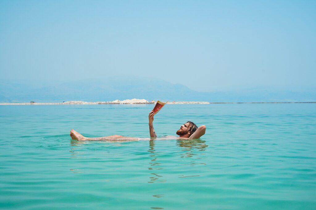 man floating in the sea while reading a book